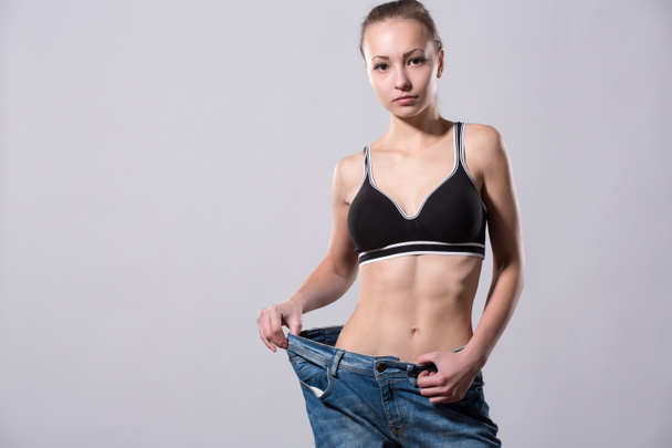 Mädchen zeigt ihren Gewichtsverlust, indem sie eine alte Jeans trägt - Foto, Bild