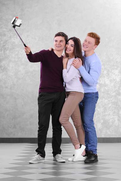 Teenager friends making photo by their self with mobile phone on grey background - Foto, Imagem