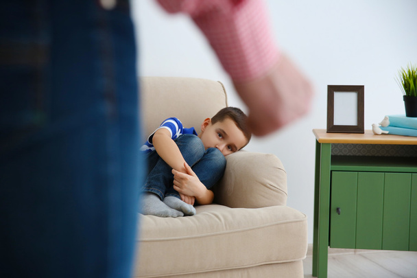 Father fist as punishment and little boy lying on sofa indoors - Photo, Image