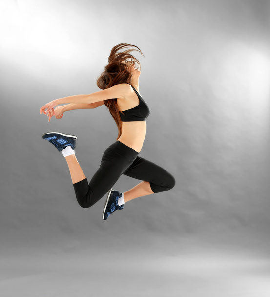 Young sporty woman jumping on grey background - Φωτογραφία, εικόνα