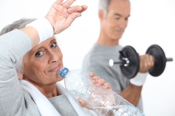 Elderly woman drinking water after gym session - 写真・画像