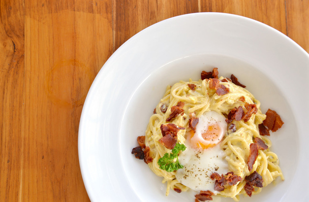 Спагетти карбонара с хрустящим беконом и яйцом на белой тарелке
 - Фото, изображение