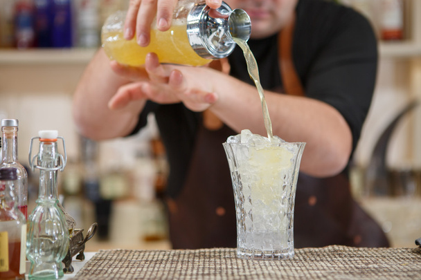 Baarimikko kaataa cocktailin lasiin baarissa
 - Valokuva, kuva