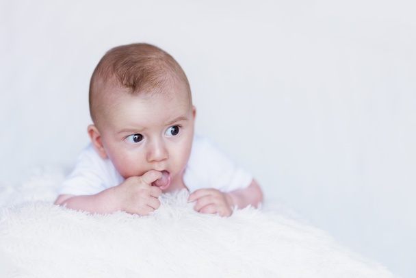 Pasgeboren Baby nieuwsgierig observeren omgeving op een zachte deken en vinger in de mond - Foto, afbeelding