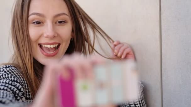 Jonge aantrekkelijke vrouw het dragen van casual zwarte en witte vacht is het nemen van selfies door haar mobiele telefoon op straat. - Video