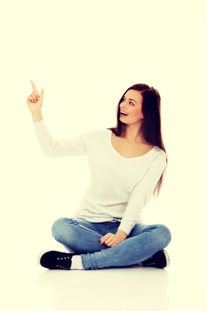 Young smiling woman sitting on the floor and pointing up - Foto, Bild