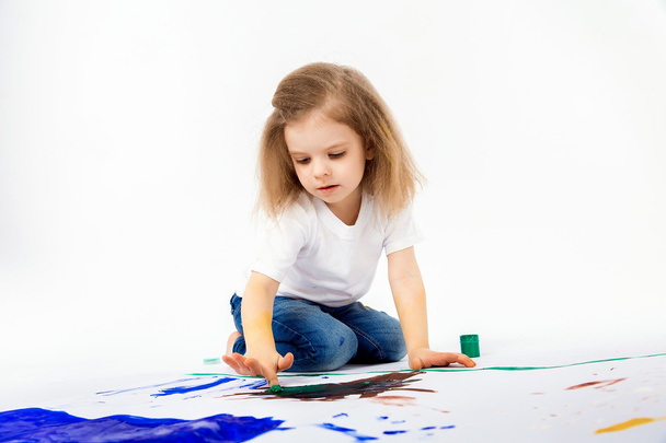 Adorable little girl, modern hair style, white shirt, blue jeans is drawing pictures by her hands with paints. Isolate. - Фото, изображение