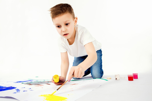 Child with paintbrush. 9 year Boy, modern hair style, white shirt, blue jeans is drawing paint brush isolated. Studio. - Фото, изображение