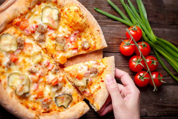 Hand picking tasty slice of pizza lying on wooden table - Foto, Imagen
