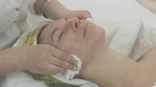 Kosmetolog wycierać kobietę twarz przez serwetkę po kosmetycznych maski w salonie piękności - Materiał filmowy, wideo