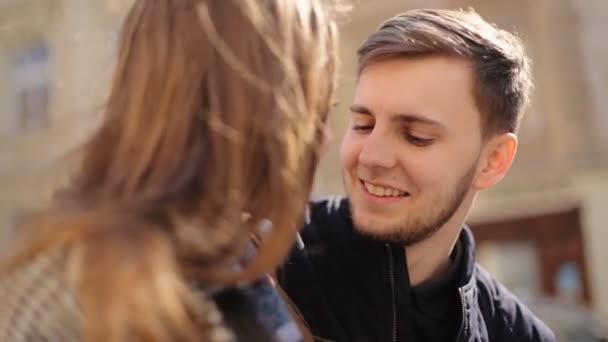 Jonge verlegen man praten met zijn vriendin zittend op het bankje op de straat. - Video
