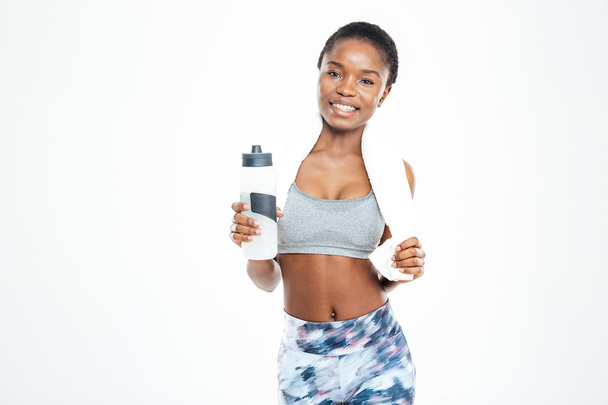 Cheerful african american sportswoman with towel holding bottle of water  - 写真・画像