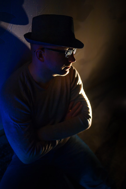 людина в окулярах і капелюх сидить у темряві
 - Фото, зображення