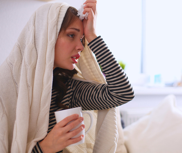 Sick woman covered with blanket holding cup of tea sitting on sofa couch - Fotó, kép
