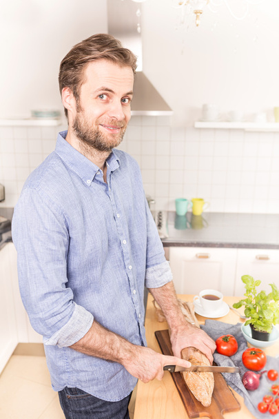 Happy caucasian man cutting bread roll in the kitchen   - Fotó, kép