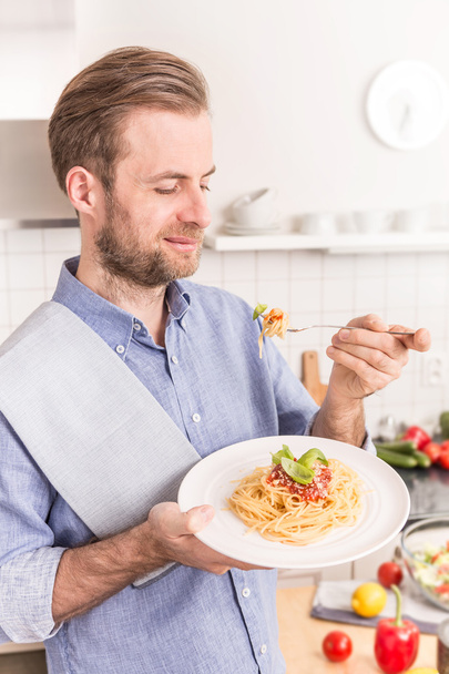 Happy smiling man eating spaghetti bolognese in the kitchen - Foto, Bild