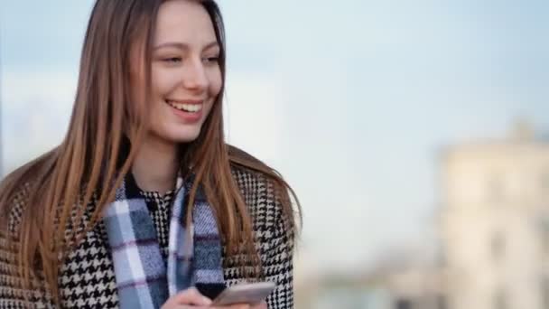 Приваблива молода жінка використовує свій смартфон і посміхається на вулиці
. - Кадри, відео