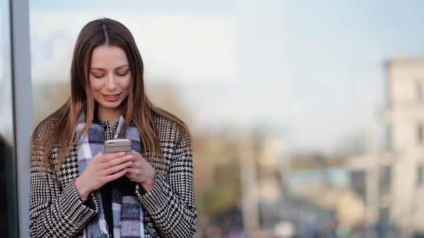 Ελκυστική νεαρή γυναίκα χρησιμοποιώντας το smartphone και το χαμόγελο στο δρόμο. - Πλάνα, βίντεο