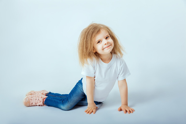 little girl 4 years old with curly hair wearing white shirt, blue jeans, pink boots sitting on the floor, smiling and looking at camera. - Valokuva, kuva