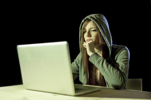 молодая привлекательная девушка-подросток в капюшоне за взлом ноутбука
 - Фото, изображение