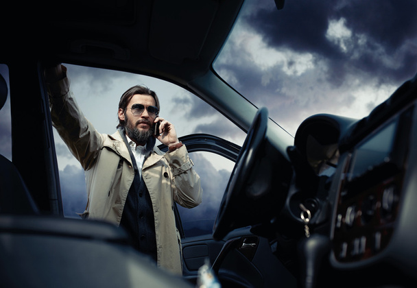 Handsome stylish man on the road next to his car talking on the  - 写真・画像