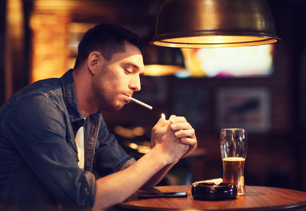 man drinking beer and smoking cigarette at bar - Фото, изображение
