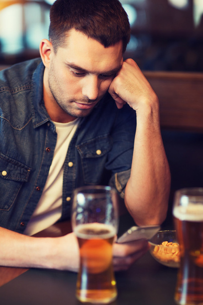 man with smartphone drinking beer at bar - Fotó, kép