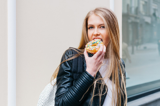Attractive young blond sexy woman eating tasty colorful donut. Outdoors lifestyle portrait of pretty girl - Foto, afbeelding