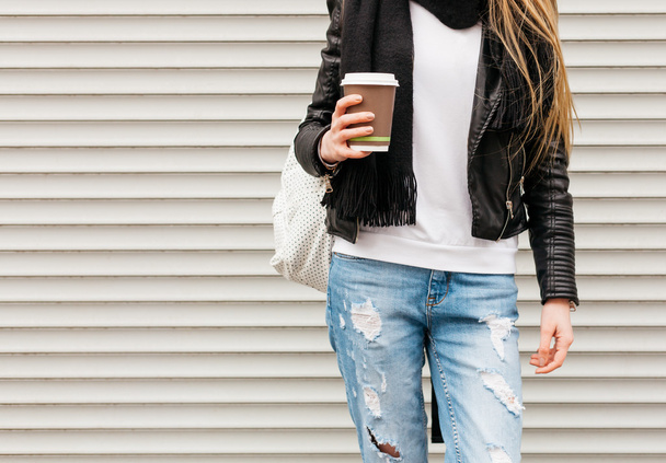 Portrait of a beautiful young blonde girl with long hair posing on a street with coffee and a backpack. Outdoor, warm color. Close up. Body parts - Zdjęcie, obraz