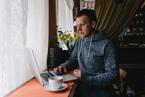 Ember használ egy laptop és cellphone-ban egy kávézó. Fiatal férfi iszik c - Fotó, kép