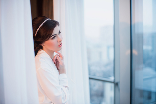 Portrait of a beautiful young girl in a white robe in the bedroom near the window - Fotoğraf, Görsel
