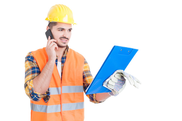 Young engineer wearing helmet with clipboard calling on cellphon - Foto, Imagen