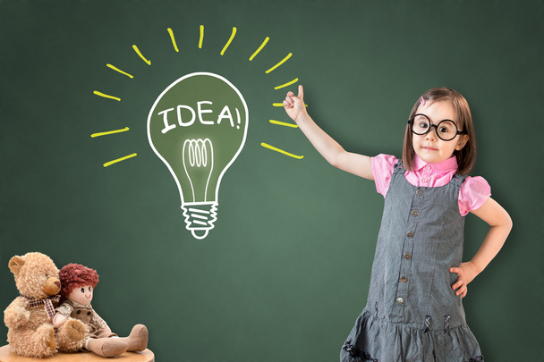 Cute little girl wearing business dress and showing a light bulb on green chalk board. - Photo, Image