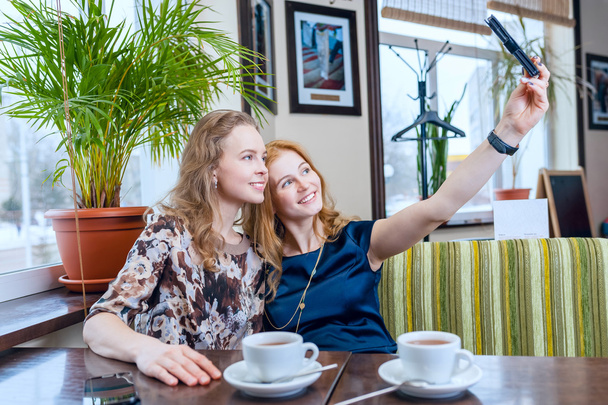 selfie. Two beautiful smiling girls photographed on a smartphone in cafe outside - Фото, зображення