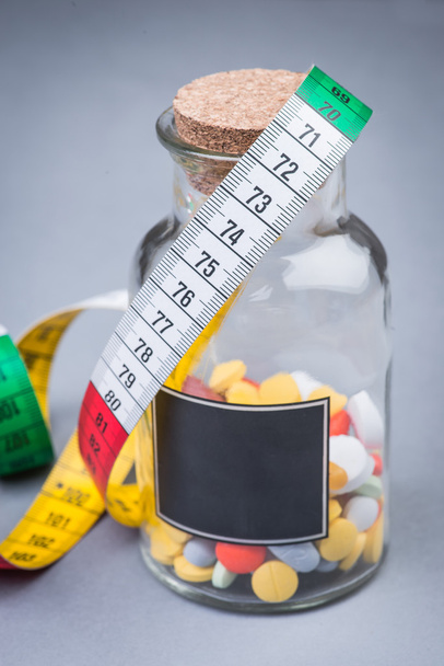 Una botella de pastillas para adelgazar con cinta métrica
 - Foto, Imagen