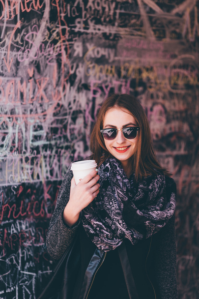 一杯のコーヒーと壁の前に立っているきれいな女の子 - 写真・画像