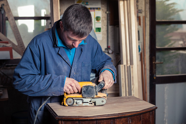 Carpintero restaurando muebles con lijadora de cinturón
 - Foto, Imagen