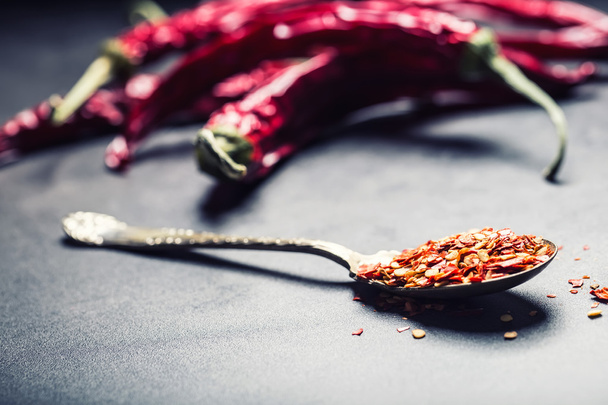 Chili. Chili peppers. Several dried chilli peppers and crushed peppers on an old spoon spilled around. Mexican ingredients - cuisine - Zdjęcie, obraz