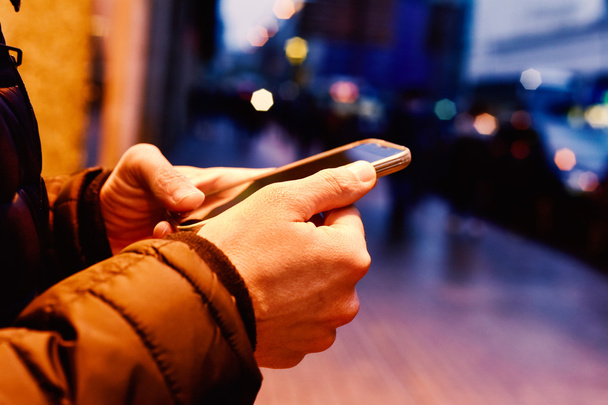 молодий чоловік використовує свій смартфон на вулиці вночі
 - Фото, зображення
