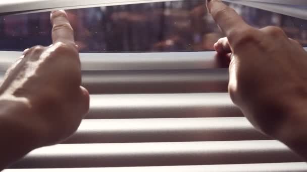 Mano femenina separando listones de persianas venecianas con un dedo para ver a través de - Metraje, vídeo