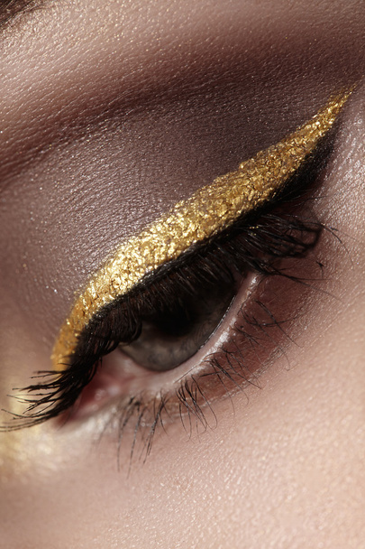 Beautiful macro shot of female eye with ceremonial makeup. Perfect shape of eyebrows, eyeliner and pretty gold line on eyelid. Cosmetics and make-up. Closeup macro shot of fashion sparcle visage - Foto, afbeelding