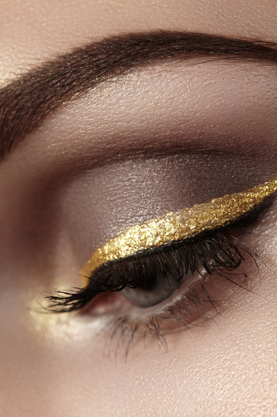 Beautiful macro shot of female eye with ceremonial makeup. Perfect shape of eyebrows, eyeliner and pretty gold line on eyelid. Cosmetics and make-up. Closeup macro shot of fashion sparcle visage - Foto, imagen