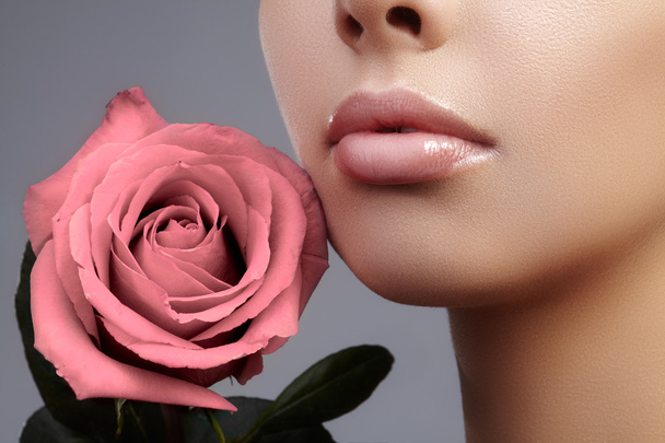 Close-up beautiful female lips with bright lipgloss makeup. Perfect clean skin, light fresh lip make-up. Beautiful spa portrait with tender pink rose flower. Spa and cosmetics - Фото, зображення