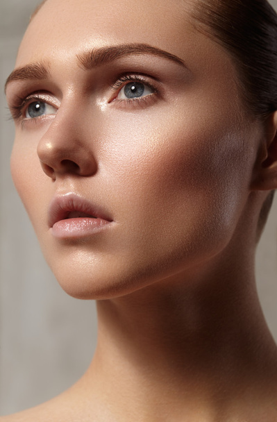 Beautiful young woman with perfect clean shiny skin, natural fashion makeup. Glamour portrait of model with cute bun hairstyle. Close-up woman, fresh spa look - 写真・画像
