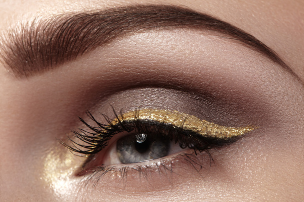 Beautiful macro shot of female eye with ceremonial makeup. Perfect shape of eyebrows, eyeliner and pretty gold line on eyelid. Cosmetics and make-up. Closeup macro shot of fashion sparcle visage - Fotografie, Obrázek