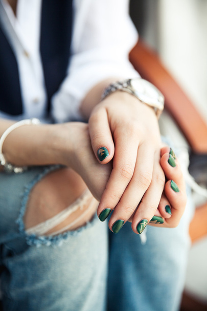 Stylish girl sitting in torn jeans and modern green nail Polish, - 写真・画像