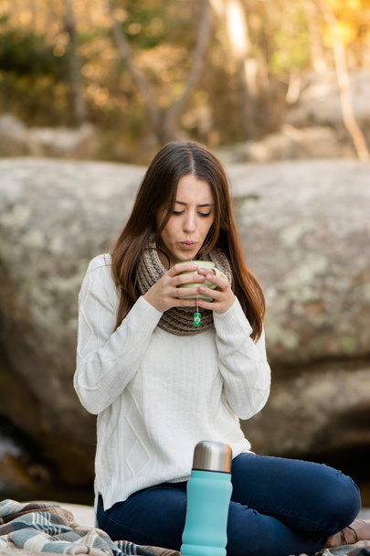 Young woman sitting on the rock, drinking tea, surrounded by nat - 写真・画像