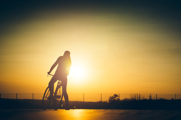 beautiful hipster girl with a bicycle on the road during sunset - Photo, Image