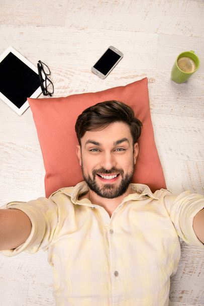Handsome man lying on the floor on pillow  and making selfie - 写真・画像