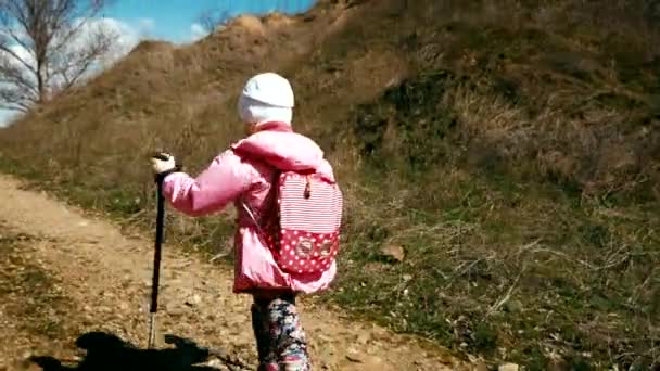 Little girl hiker in a pink jacket with a backpack and trekking poles walks in the canyon - Felvétel, videó